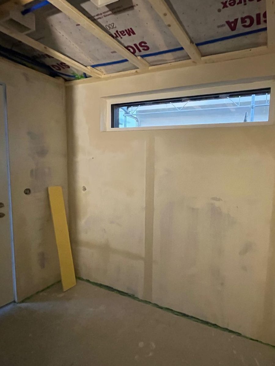 Eingangsbereich im Rohbau, Blick zum Eingang, mit unbehandelten Gipsplatten, offener Deckenkonstruktion und sichtbaren Spachtelstellen